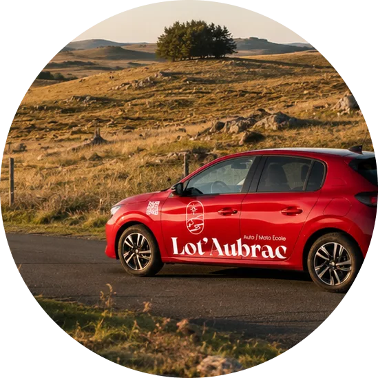 Voiture d'auto-école floquée Lot'Aubrac sur une route du plateau de l'Aubrac